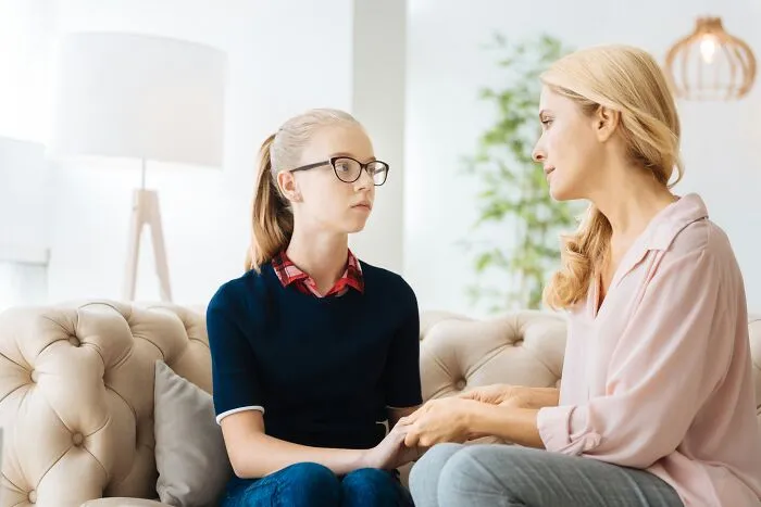 A mother talking intently to her teenage daughter on a couch, representing dynamic with narcissistic parents.
