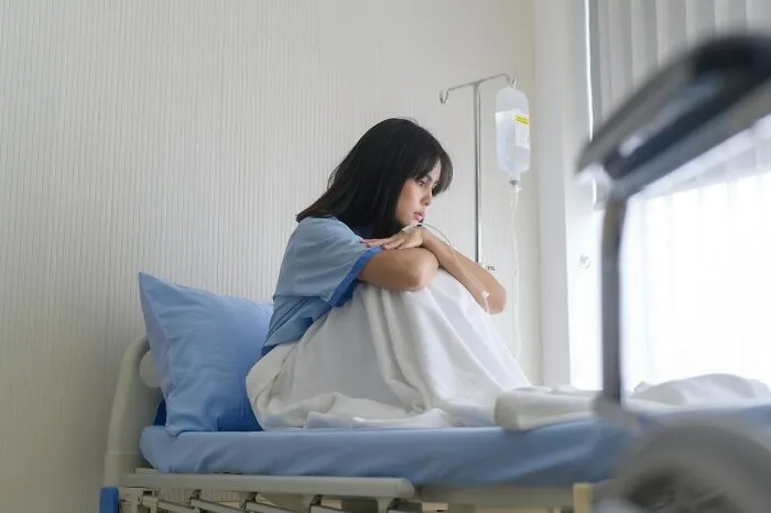 A thoughtful woman sitting on a hospital bed, reflecting on misconceptions about women's bodies.