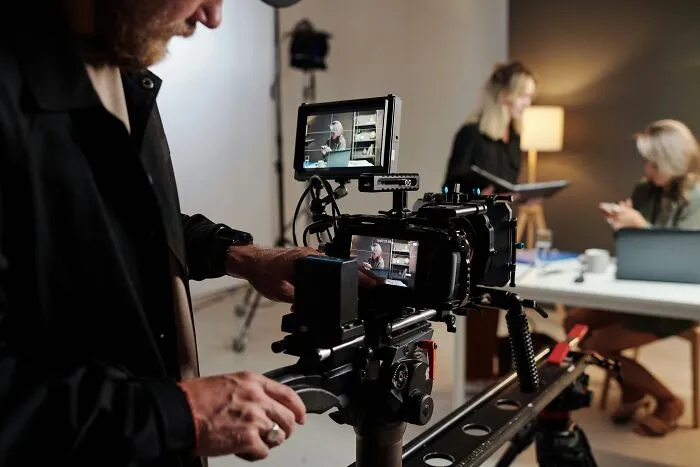 Behind the scenes camera operator filming a video production crew in a studio setting.