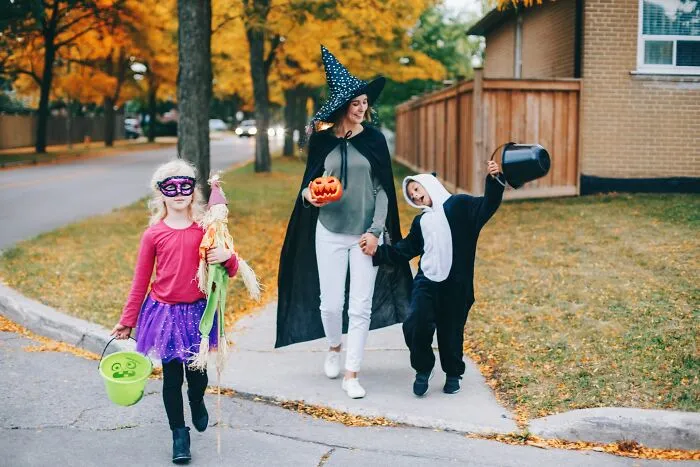 Family in Halloween costumes walking together while trick-or-treating in the neighborhood