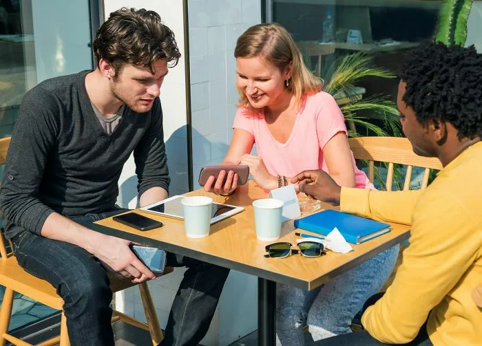 A group of friends sitting together outdoors looking at a phone, discussing behaviors they refuse to tolerate.
