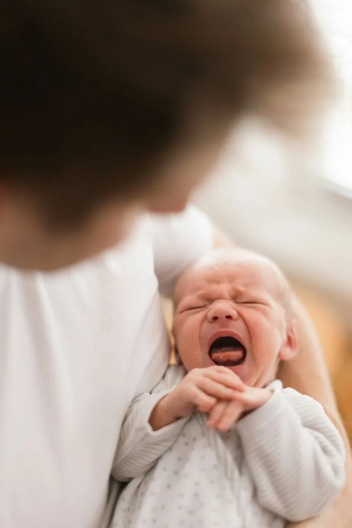 An adult holding a crying baby who might be traveling with parents.