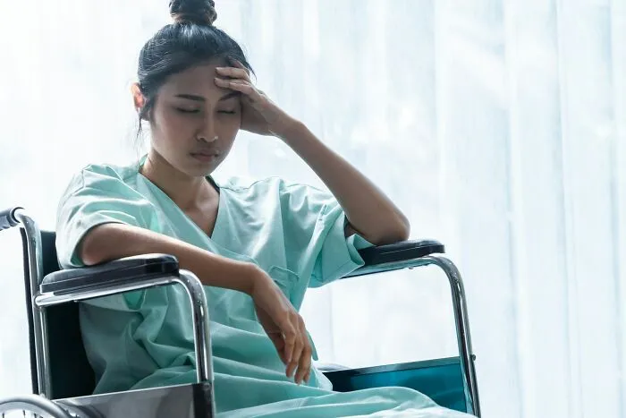 Woman in hospital gown sitting in wheelchair looking distressed and worried