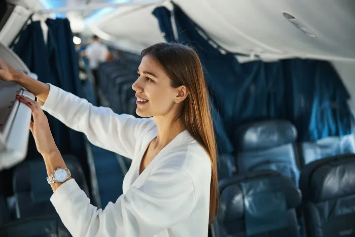 A woman smiles while placing her hand luggage into the overhead bin on flights