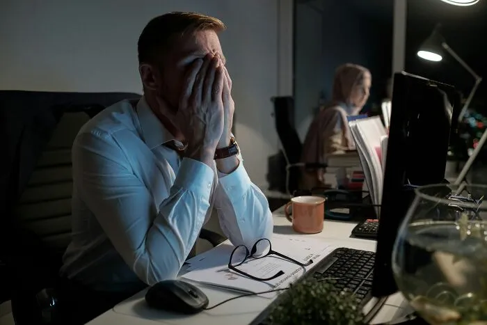 Tired employee covering face while working late on a computer