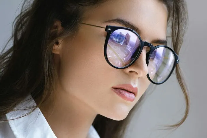 Close-up of a woman wearing black-framed glasses with screen reflections, showing a smart life tips style.