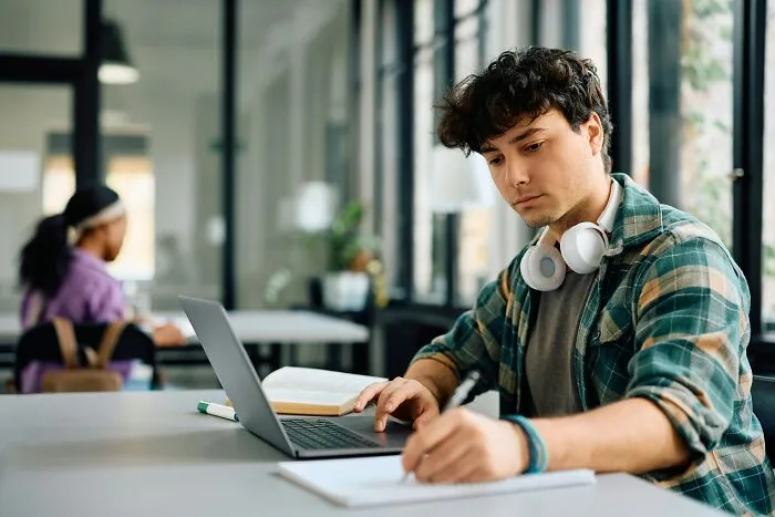 Focused student using laptop and taking notes in library