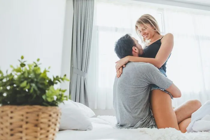 A man holding a woman lovingly on a bed highlighting misconceptions about women's bodies.