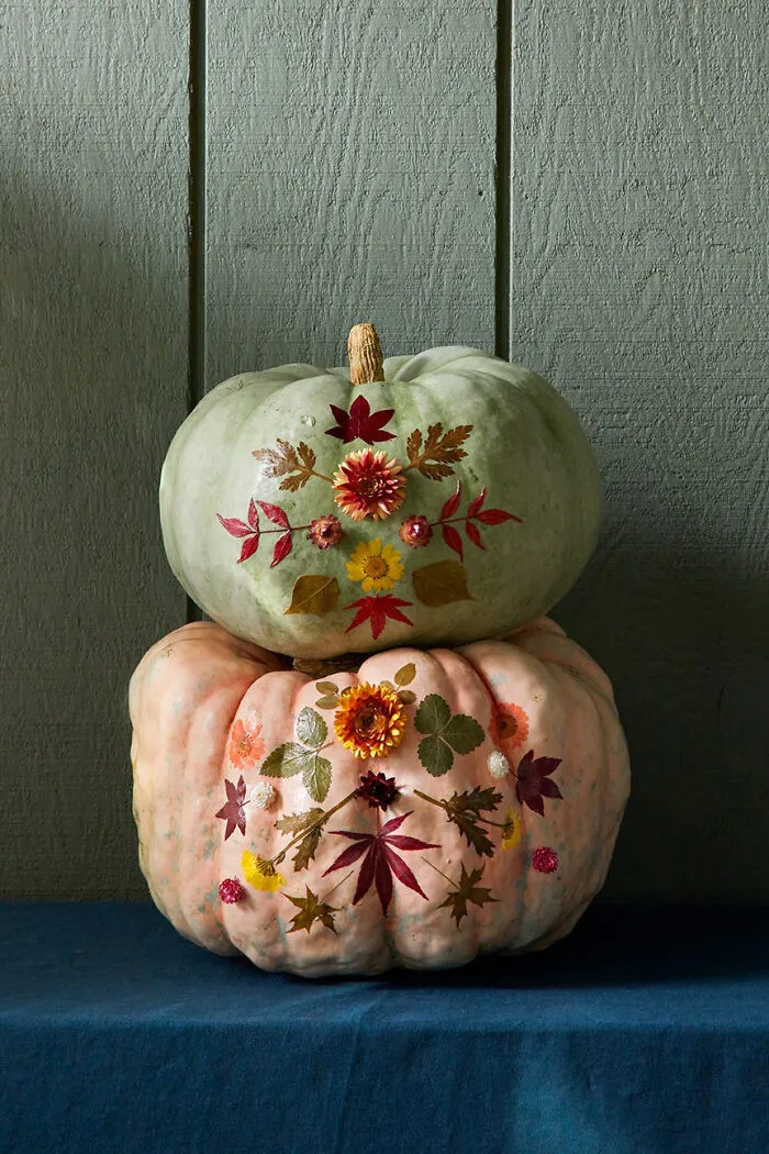 Two stacked pumpkins decorated with pressed flowers and leaves for creative Halloween decor.