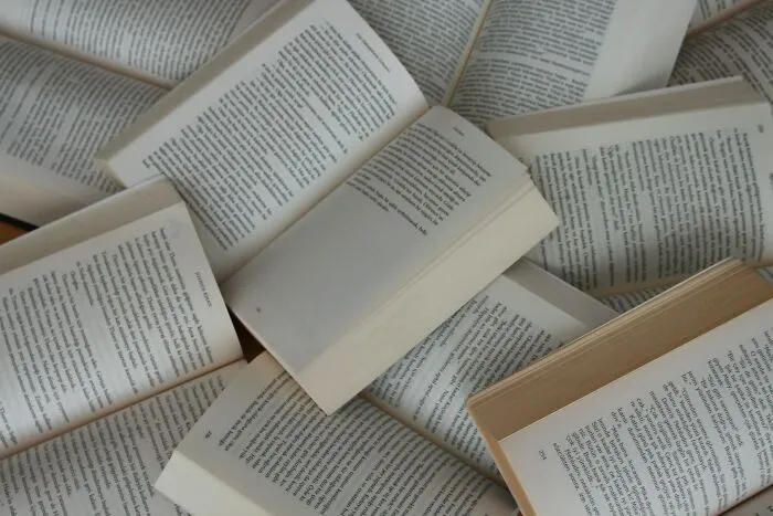 Pile of open books with visible printed text scattered on a surface