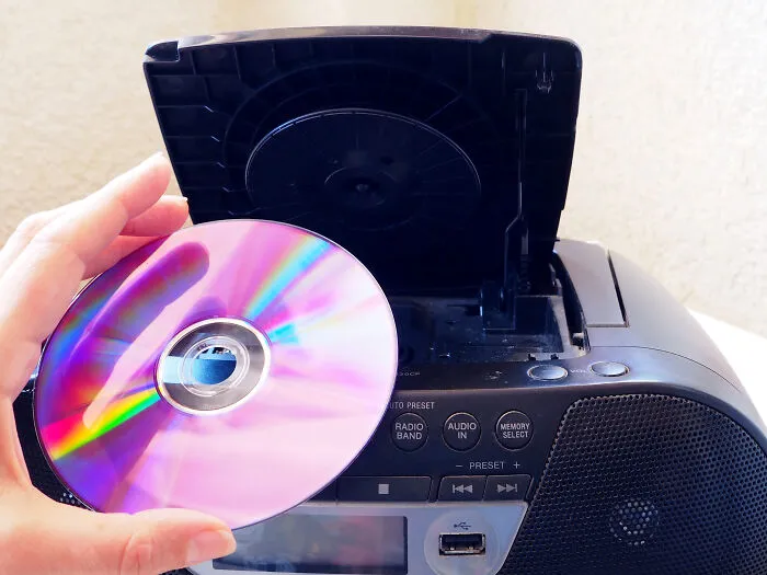 A hand loading a compact disc into a portable boombox player during a funeral mishap.