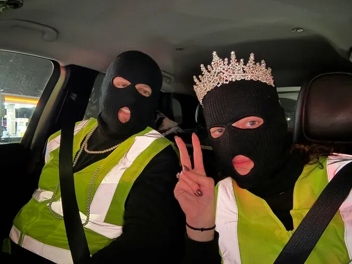 Couple in ski masks and safety vests sharing creative Halloween costume ideas in a car