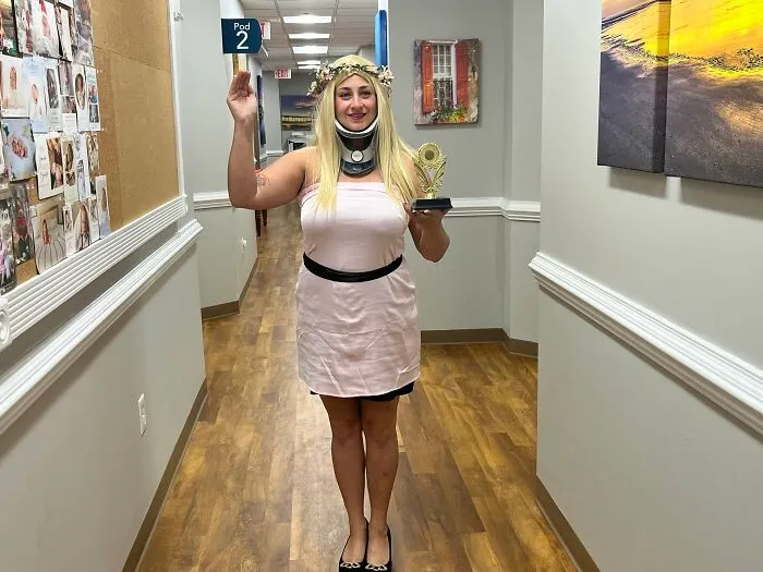Woman wearing a neck brace and holding a trophy as a creative Halloween costume idea in an office.