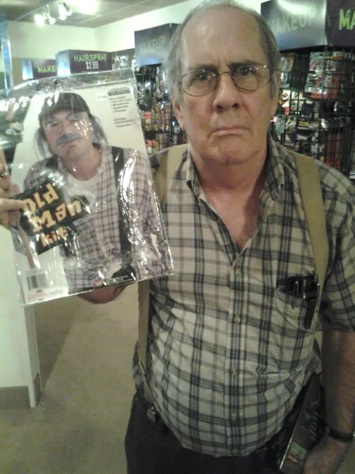 An older man holding an old man Halloween costume kit in a store