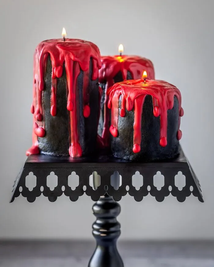 Tall black pillar candle cakes dripping with red frosting icing featured as spooky Halloween foods.