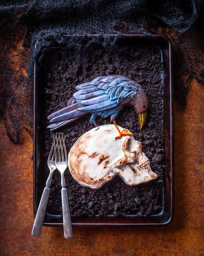Detailed edible raven perching on a human skull dessert served on cookie crumbles for Halloween foods.