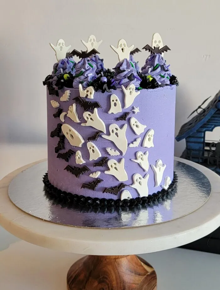 A tall purple frosted cake decorated with white ghosts and black bats for creative Halloween foods.