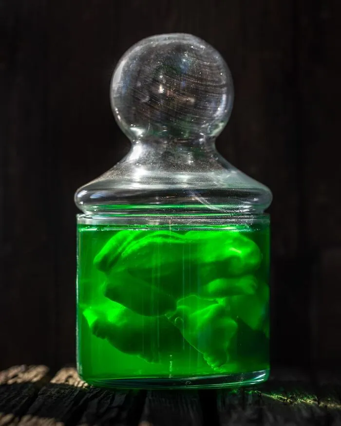 Eerie bright green potion jar with floating candy shapes for spooky Halloween foods.