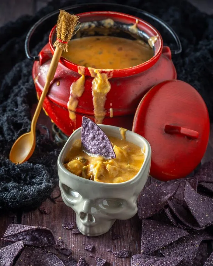 Spooky Halloween foods with cheese dip served in a red cauldron and skull cup.