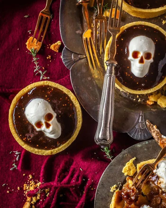 Mini Halloween foods featuring dark tarts decorated with white edible skull toppers.