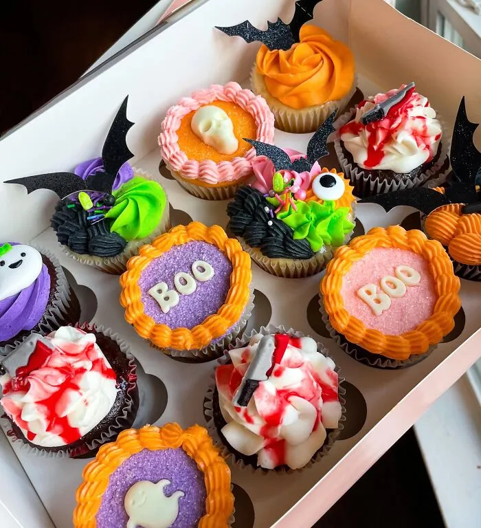 An assortment of spooky Halloween foods including cupcakes topped with sugar skulls, bat wings, and fake blood.