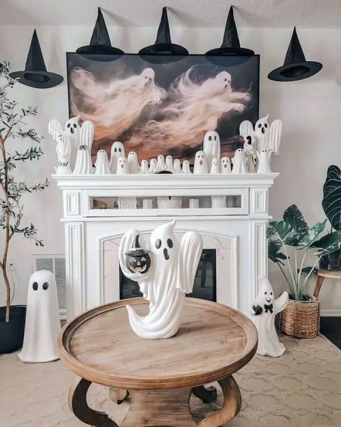 White fireplace mantle decorated with spooky ghost figurines and floating witch hats for Halloween.