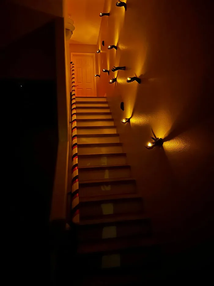 Hands reaching from a staircase wall holding small candles for Halloween.