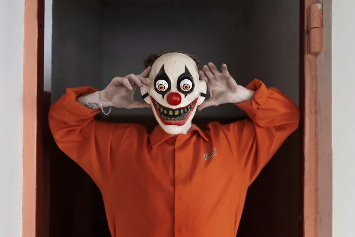 Person wearing creepy clown mask in orange outfit for haunted house stories