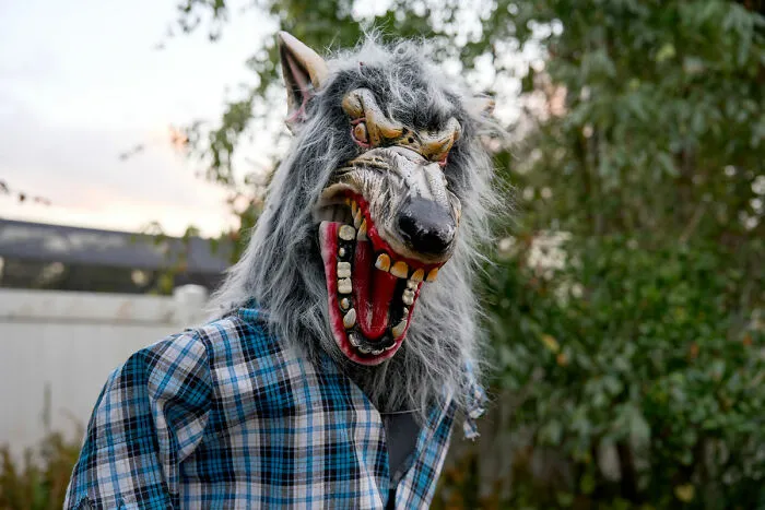 Person wearing scary werewolf mask outdoors near haunted house
