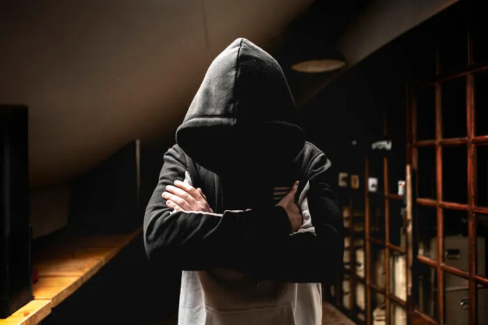 Mysterious hooded figure in dark room with arms crossed