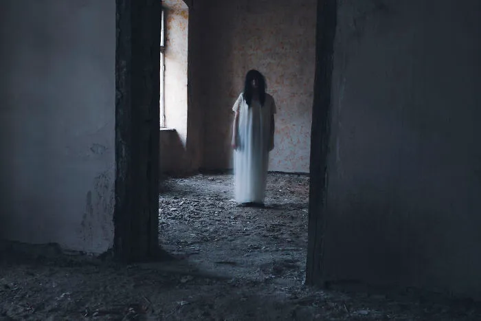 Ghostly figure in white dress standing in dark haunted house room