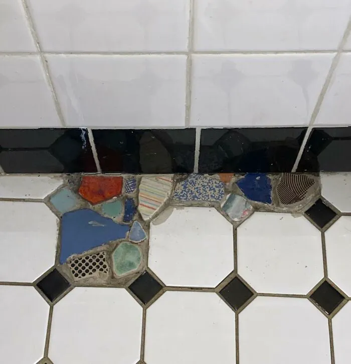 A tiled bathroom floor repaired with a mosaic of colorful broken ceramic pieces using creativity.