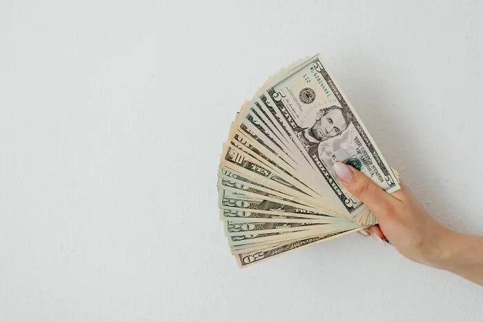 Hand holding a fan of dollar bills, showcasing practical money-saving tricks that build savings.