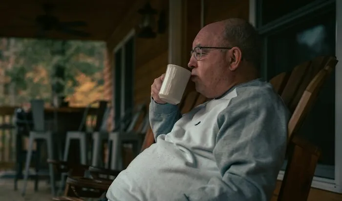 Senior man drinking coffee on a porch, relaxing using smart money-saving tricks for retirement.