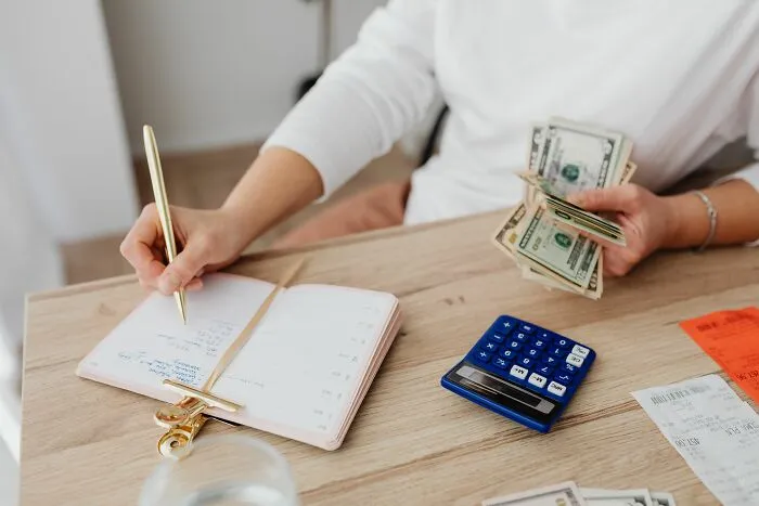 Person counting cash while budgeting on a notepad, demonstrating smart money-saving tricks.