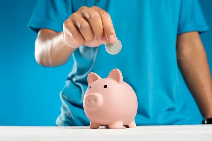 A person putting a coin into a pink piggy bank to demonstrate effective money-saving tricks.