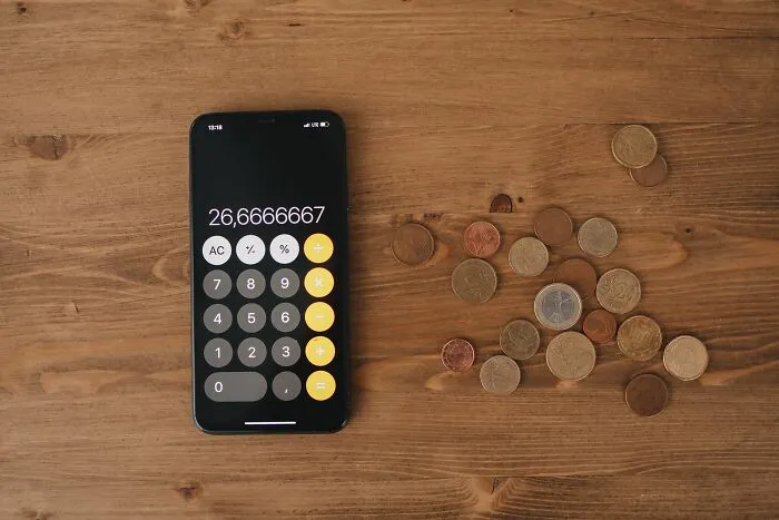 A smartphone displaying a calculator app next to coins to calculate money-saving tricks.