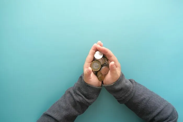 Top view of hands holding a pile of coins, illustrating effective money-saving tricks to grow savings.