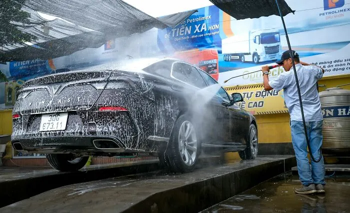 A man washing his black car at a station, demonstrating simple money-saving tricks for vehicle care.