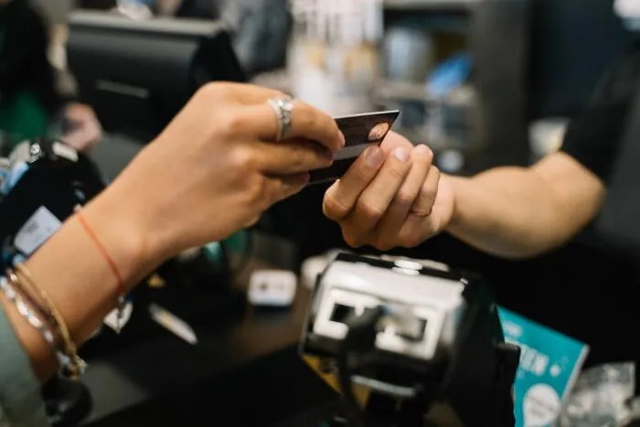 A customer handing over a credit card to make a payment, highlighting everyday money-saving tricks