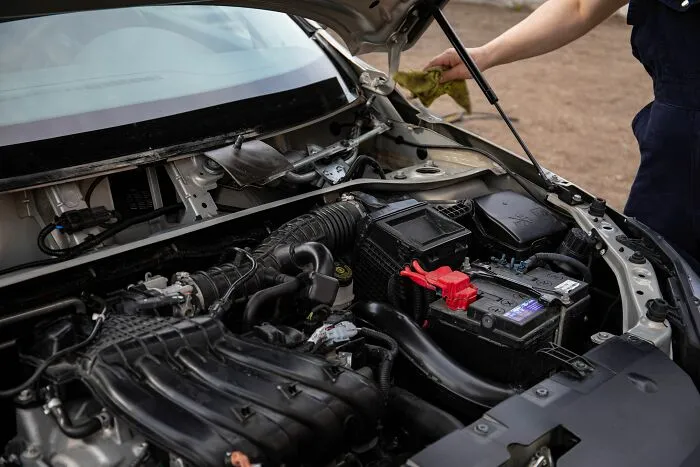Mechanic inspecting an open car engine compartment to demonstrate DIY money-saving tricks