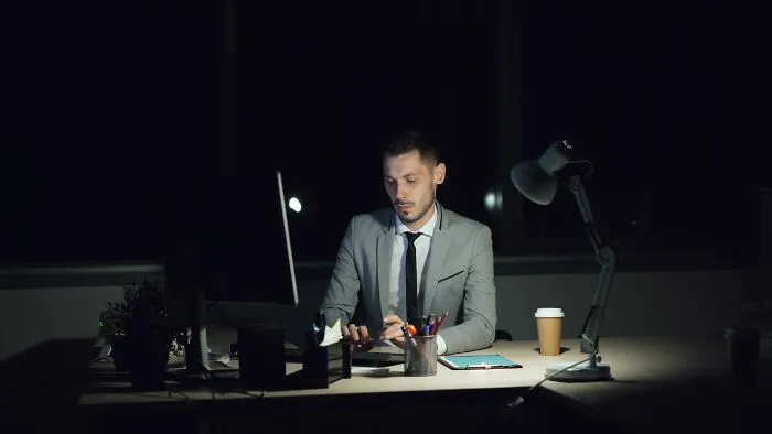 Man working late at a illuminated computer desk applying money-saving tricks to cut expenses