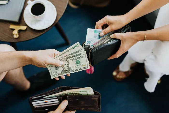 Hands holding wallets and cash representing smart money-saving tricks