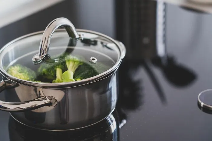 Pot with fresh broccoli cooking on an induction stove using energy money-saving tricks.