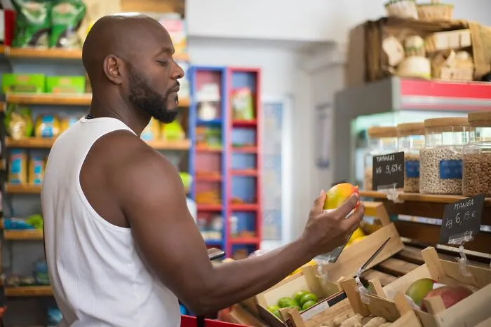 Man inspecting fresh produce at a grocery store applying budget money-saving tricks.