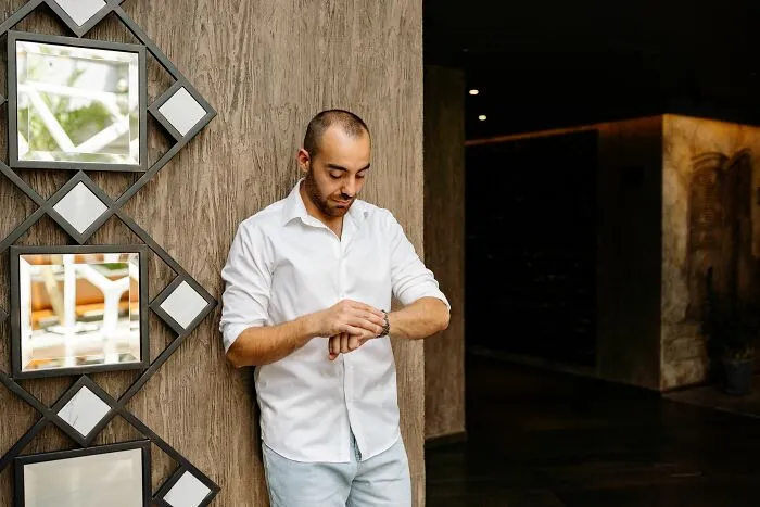 A man looking at his watch while leaning on a wall, showing how time management relates to money-saving tricks