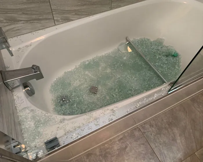A bathtub filled with shattered glass from a broken shower door during a home renovation
