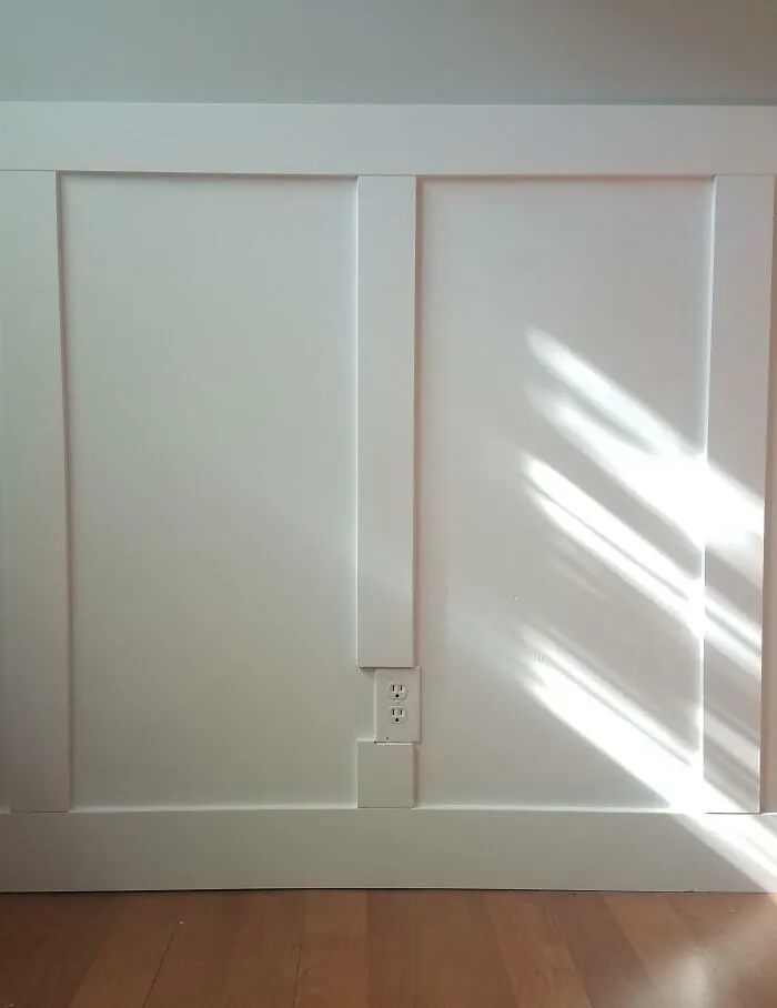 A poorly planned wainscoting home renovation showing an outlet cut into the wood panel.