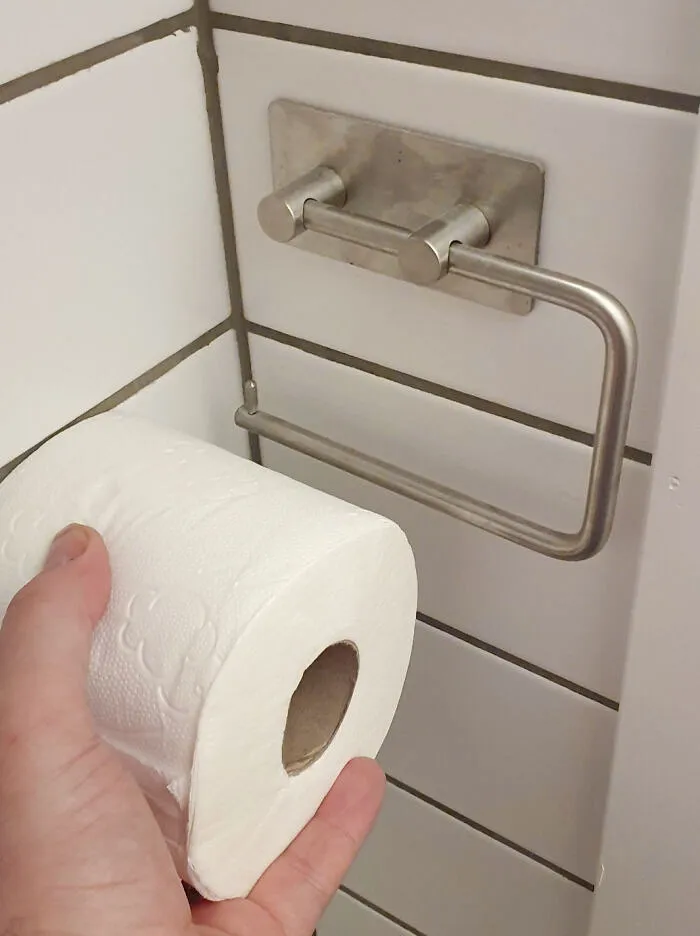A poorly planned bathroom renovation fiasco with a toilet paper holder installed too close to a tiled wall.