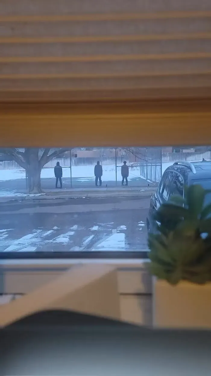 Creepy photos from a window showing three mysterious hooded figures standing in a snowy field at dusk.